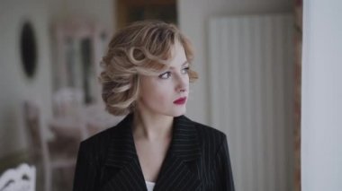 Pencerenin önünde durup lüks bir evde poz veren düşünceli bir kadının portresi.