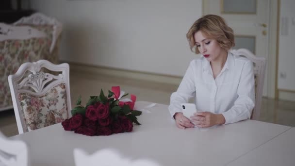 Portret romantycznej pani wykorzystuje telefon przy stole z bukietem róż — Wideo stockowe