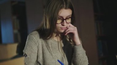 Kitaplardan bilgi toplayan, kütüphanede düşünen ve gülümseyen genç bir kız.