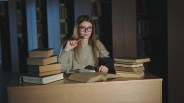 Çalışma masasında kitaplarla uğraşırken elinde kalemle düşünen çalışkan bir öğrenci.