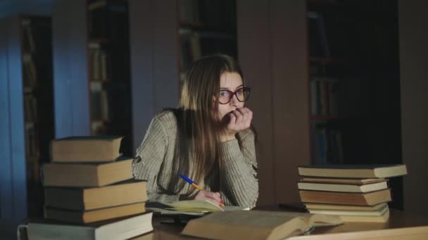 Chica observando el compendio de los libros en un escritorio y mirándolo a media luz — Vídeo de stock