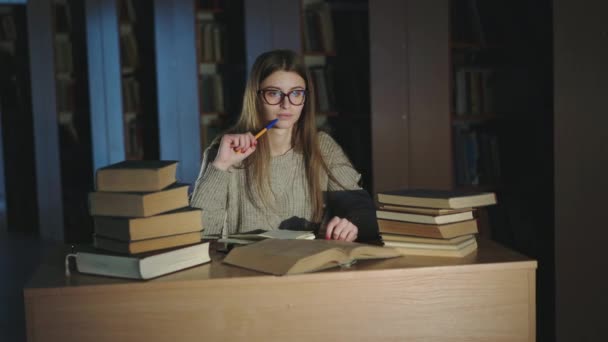 Estudiante diligente con pensamiento de pluma en mano durante el trabajo con libros en el escritorio — Vídeo de stock