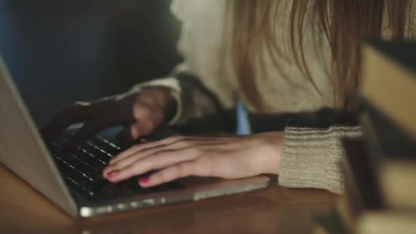 Zicht op vrouwelijke handen typen op laptop toetsenbord op bureau met boeken op dimlicht — Stockvideo