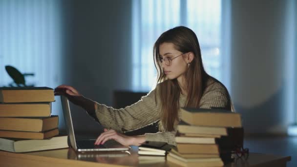 Menina cansada fecha laptop, tira óculos e se inclina na mão na mesa com livros — Vídeo de Stock