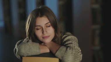 Enigmatik kız öğrenci masanın üzerindeki kitap yığınına yaslanmış, kameraya gülümsüyordu.