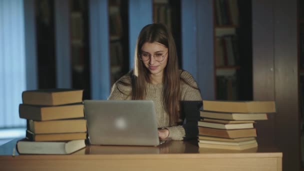 Estudiante trabajando con laptop, regocijándose, levantando las manos y riendo en la biblioteca — Vídeo de stock