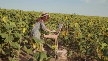 Güzel kızıl saçlı bayan yaz ayçiçeği tarlasında resim yapıyor.