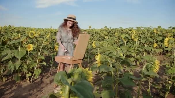Uitstekend uitzicht op een mooi meisje die een landschap schildert in het zonnebloemveld — Stockvideo
