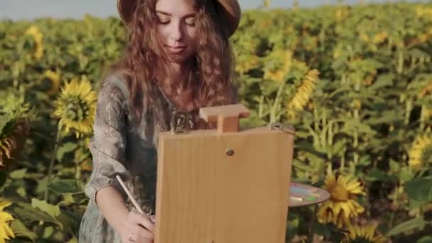 Porträt einer glücklichen Frau mit lockigem Haar, die inmitten eines bunten Sonnenblumenfeldes malt — Stockvideo