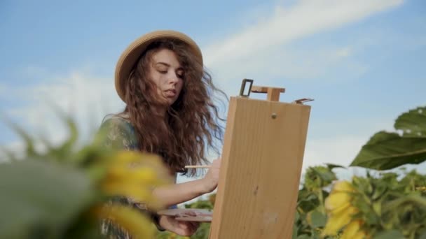 Sorrindo artista feminina pintura entre girassóis em vista céu brilhante — Vídeo de Stock