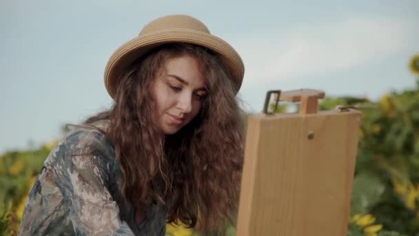 Vrolijke langharige dame schilderen landschap met aquarellen onder zonnebloemen — Stockvideo