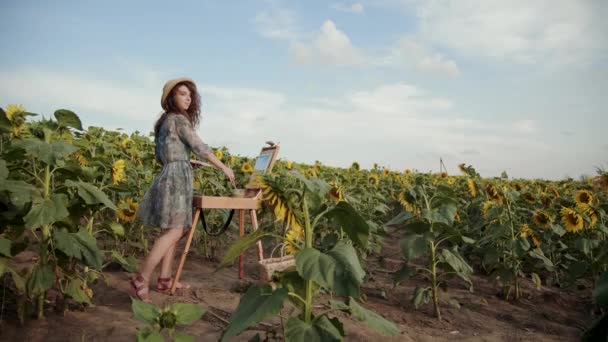 Bastante artista femenina mirando alrededor del amplio campo de girasol durante la pintura — Vídeo de stock