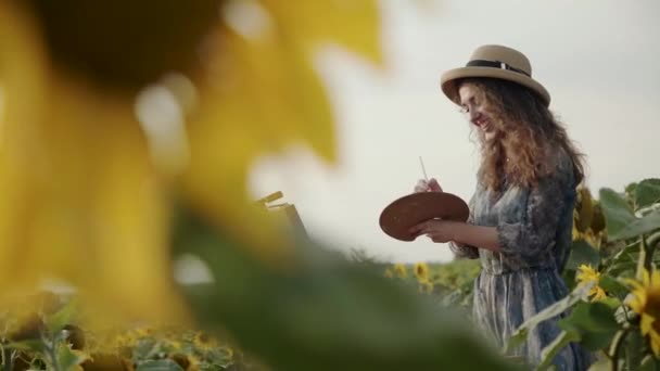 Vista al girasol de chica alegre en sombrero con el pelo largo que sopla durante la pintura — Vídeo de stock