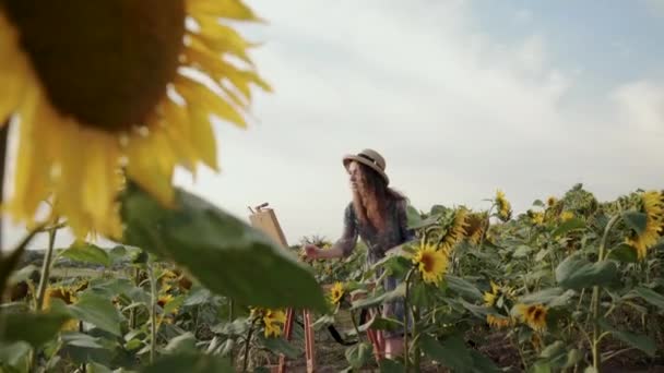 Hermosa dama pintando paisaje entre girasoles con cielo de verano brillante — Vídeos de Stock