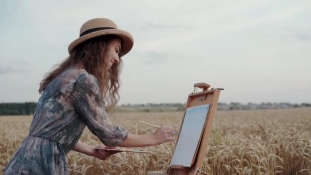 Gelukkig dame in hoed en jurk schilderij landschap op doek tussen tarweveld — Stockvideo