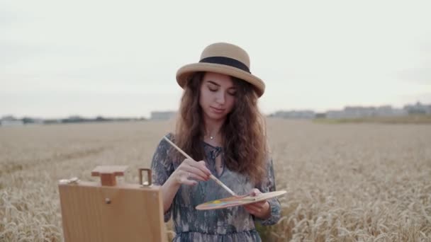 Pintura de paisaje feliz de la pintura en la lona entre el campo de trigo maduro con horizonte — Vídeos de Stock