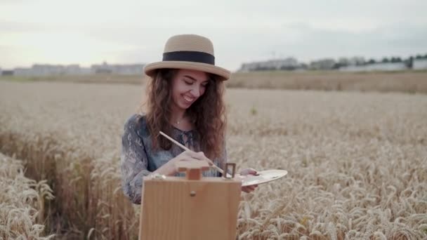 Joyeux jeune femme dans la peinture chapeau avec aquarelles parmi le blé mûr — Video