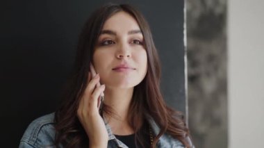 Güzel esmer telefonda konuşuyor ve kameraya gülümsüyor.