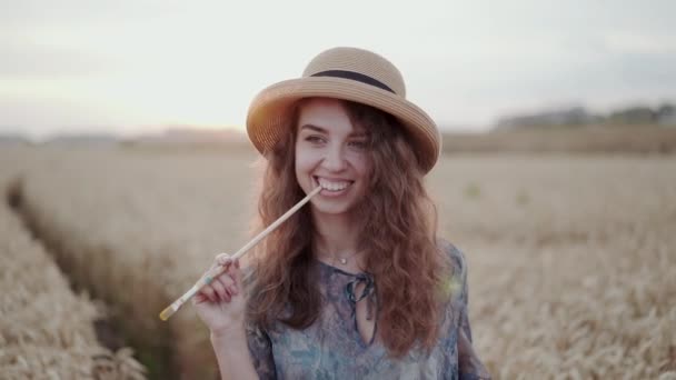 Porträt der hübschen Dame mit Hut spielt mit Pinsel und lächelt zwischen Feld — Stockvideo