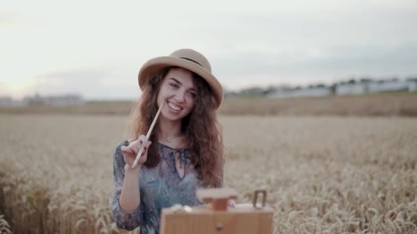 Portret van mooie dame in hoed poseert met penseel en glimlacht tussen het veld — Stockvideo