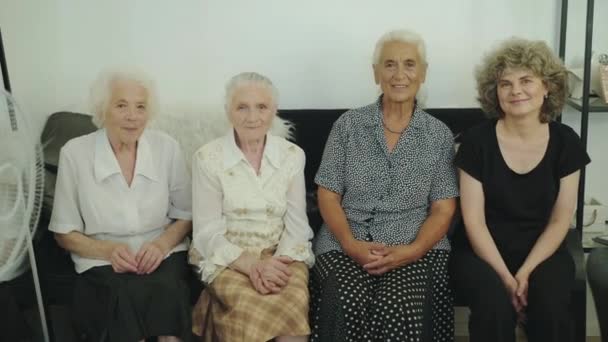 Retrato de cuatro mujeres de edad mixta en el sofá mirando y sonriendo a la cámara en la habitación — Vídeo de stock