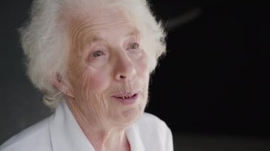 Arka planda hafif bir gülümsemeyle kameraya konuşan son sınıf güzeli bir kadın.