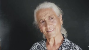 Neşeli, parlak gözlü, arka planda gülücükle kameraya bakan büyük anne.