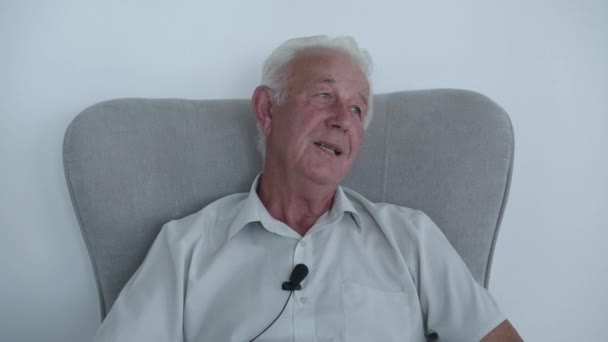 Uomo anziano seduto sulla poltrona in camera e parlare con il sorriso sul viso — Video Stock