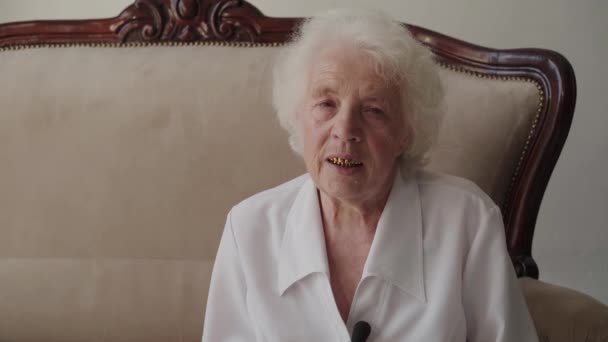Portret starszej kobiety siedzącej na kanapie w pokoju i rozmawiającej przed kamerą — Wideo stockowe