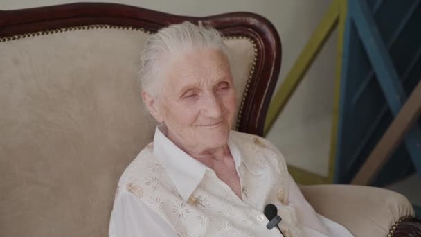 Ritratto di nonna carina seduta sul divano in camera e che parla alla macchina fotografica — Video Stock