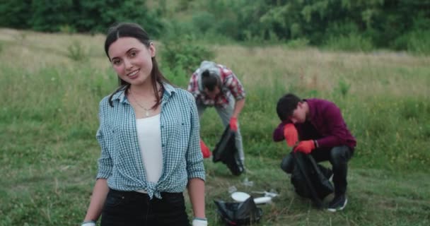 Šťastná dívka zkříží ruce, usmívá se na kameru na lidi sbírající odpadky — Stock video