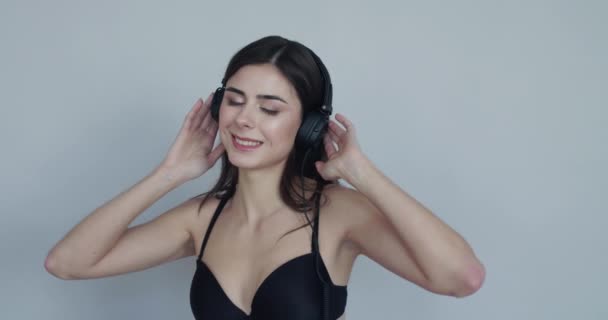 Menina com fones de ouvido, tocando os auriculares, balançando a cabeça e sorrindo — Vídeo de Stock
