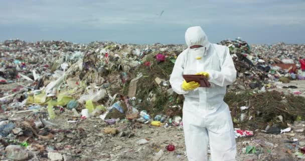 Ökologe im Schutzanzug macht sich Notizen in seinem Tablet bei der Untersuchung einer Deponie — Stockvideo