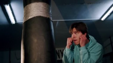 Yalnız boksör ağır çekimde kum torbasına vurur. Genç adam içeride antrenman yapıyor. Spor salonunda güçlü bir atlet. Spor konsepti.