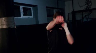 Yalnız boksör, ağır çekimde karanlık spor salonunda boks hareketlerini geliştirir. Genç adam içeride antrenman yapıyor. Spor salonunda güçlü bir atlet. Spor konsepti.