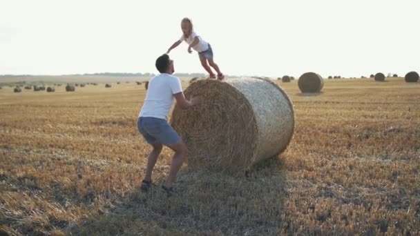 Kleine dochter springen op vaders armen van een grote haycock in het veld — Stockvideo