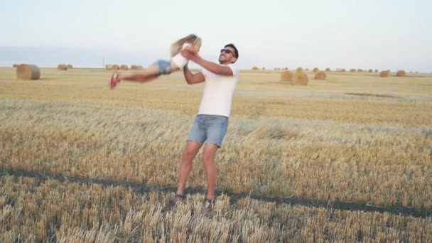 Feliz padre gira a su hija en las manos en un campo con rastrojos — Vídeos de Stock