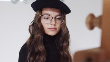 Bere takmış genç bir kadın ressamın, resim stüdyosundaki tuvale resim çizmesini yakından çek.