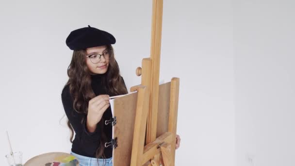 Young woman artist in beret painting picture on canvas in art studio — Stock Video