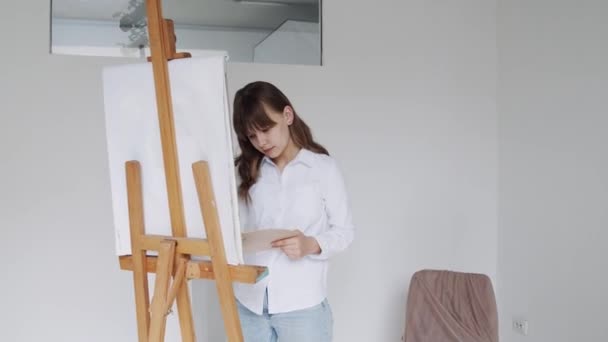 Девушка-художник рисует картину на холсте в художественной студии — стоковое видео
