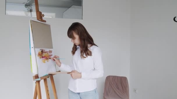 Νεαρή καλλιτέχνης κορίτσι ζωγραφική εικόνα σε καμβά στο στούντιο τέχνης — Αρχείο Βίντεο