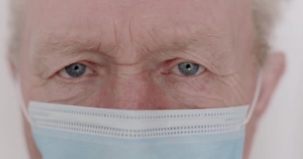 Macro guardare in macchina fotografica di uomo anziano rugoso con tristi occhi blu e maschera — Video Stock