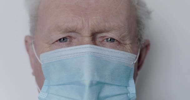 Makro přibližující se modrookého dědečka se dívá do kamery s lékařskou maskou — Stock video