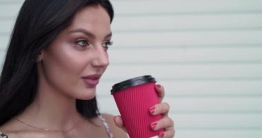 Çekici esmer, saç kesen, kameraya hafifçe gülümseyen ve içecek içen.