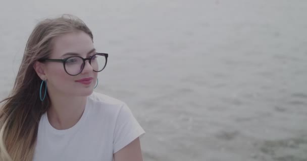 Menina em óculos com cabelo soprando regozijando-se ao olhar para o céu em ondas do rio — Vídeo de Stock