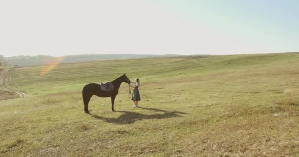 Slaviska kvinna i en nationell klänning står vid en häst och beundrar den bland stäpper — Stockvideo