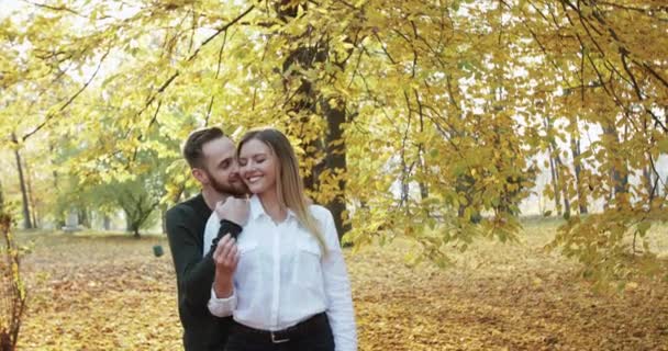 Lovely man embraces his girl and kisses her in neck in autumn park — Stock Video