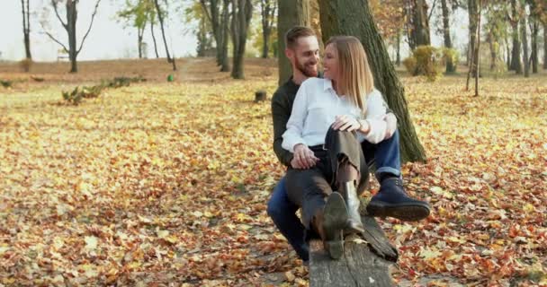 Счастливая, прекрасная пара, отдыхающая в объятиях и целующаяся на скамейке в парке — стоковое видео
