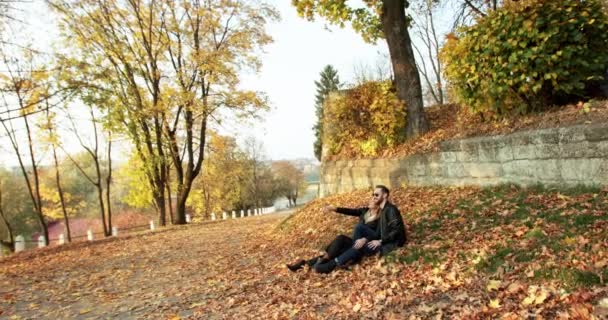 Прекрасний осінній вид з парою закоханих відпочиває на газоні, покритому листям — стокове відео