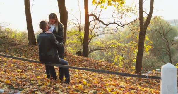Romantisch meisje zoenen haar man op hek in de herfst park met zon schijnt — Stockvideo